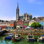 Colorful buildings and old boats with cathedral in background in the harbor of Cobh, County Cork, Ireland